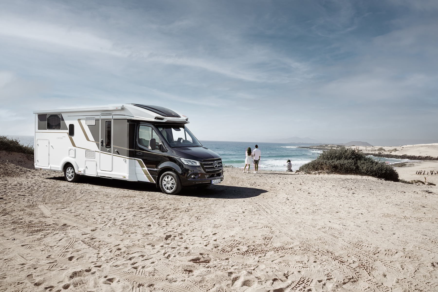 Camping-car sur la plage, à côté de quelques personnes et la mer en arrière-plan.